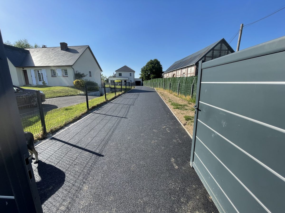 Longue allée en enrobé bordée de haies menant à une maison normande